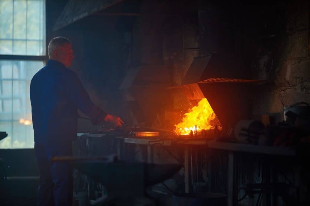 Industrial worker handling stainless steel near a high-temperature furnace