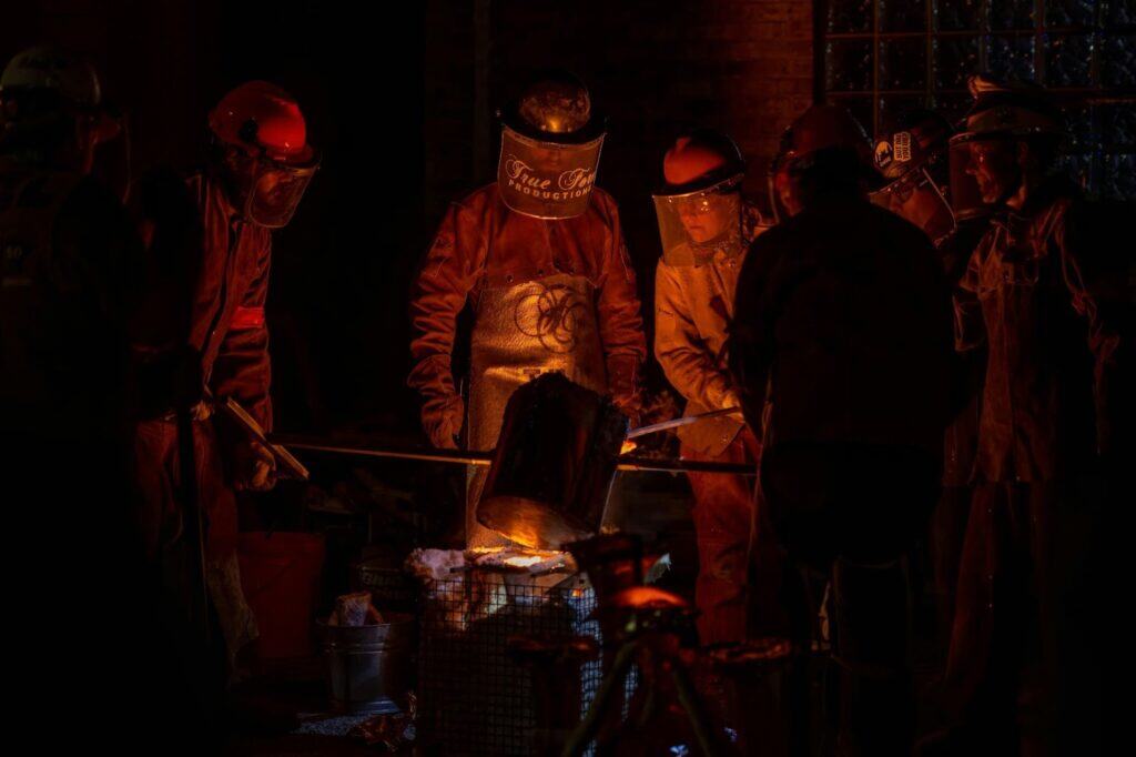 Foundry workers carefully pouring hot molten metal while making heat resistant steel parts